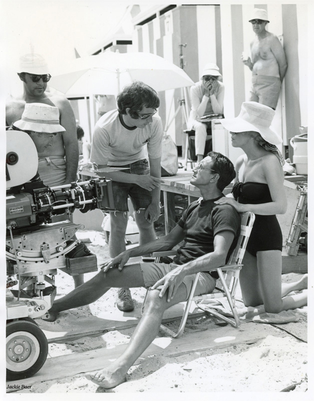 Photo en noir et blanc du tournage, avec le réalisateur et un acteur sur la plage