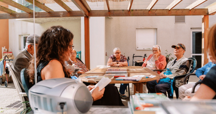 groupe de personnes âgées écoutant une femme qui lit un livre sous une pergola